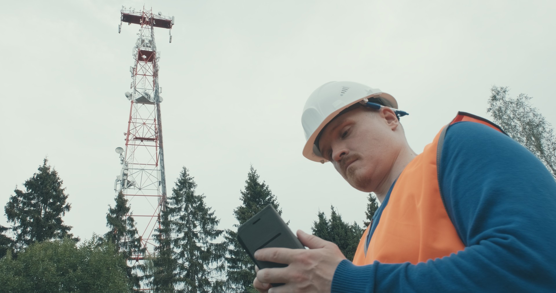 4G 5G cellular radio tower, worker in overalls and helmet is standing next to it